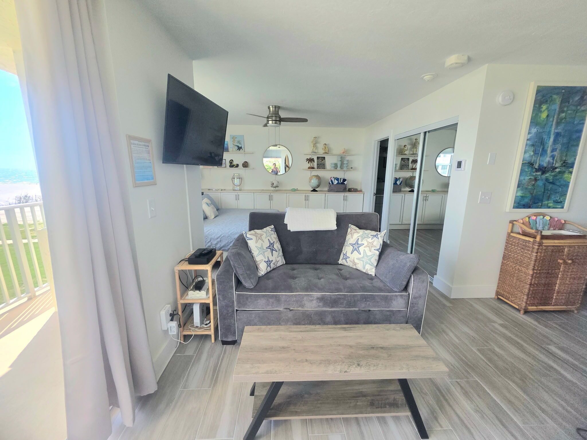 Un moderno salón con un sofá gris, una mesa de centro de madera y un televisor de pantalla plana montado en la pared.