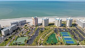 A coastal hotel complex with multiple high-rise buildings, a beach, parking areas, and tennis courts. - Beachfront w Stunning Views Modern Bright (Fort Myers Beach)