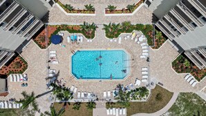 An aerial view of a hotel with a central swimming pool surrounded by lounge chairs and sunbeds, with palm trees and a landscaped garden. - Beachfront w Stunning Views Modern Bright (Fort Myers Beach)