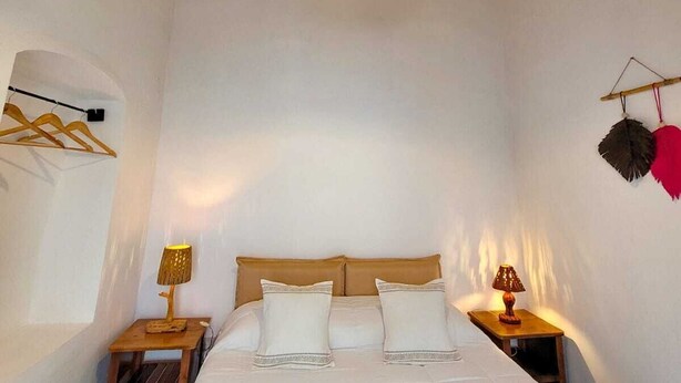 Une chambre avec un plafond en bois, un lit avec une literie blanche, une lampe suspendue et une petite table de chevet avec une lampe.