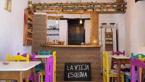 Un intérieur rustique avec des poutres en bois, un panneau noir sur lequel on peut lire « LA YIEJA ESQUINA », et des chaises aux couleurs vives.