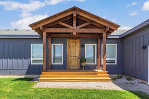 A two-story building with a wooden porch, a front door, and two windows on the ground floor.