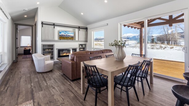 A spacious living area with a fireplace, a dining table with chairs, and a view of a snowy landscape through large windows.