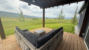 A covered outdoor seating area with a view of a grassy field and distant mountains. - New! Otter Loop Retreat - Near Grand Targhee (Driggs)