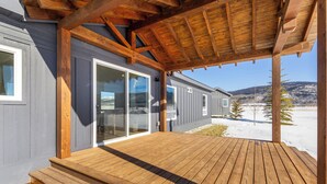 A wooden deck with a covered area and a sliding glass door leading to a building.