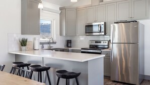 A modern kitchen with grey cabinets, stainless steel appliances, a large island with bar stools, and a view of the outdoors.