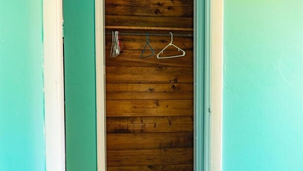 Un armario de madera con una puerta blanca, dos perchas blancas y una pared azul.