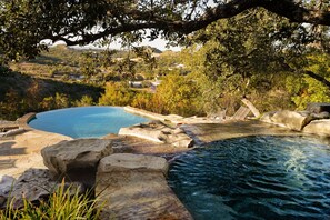 Un espace piscine agrémenté de formations rocheuses naturelles et offrant une vue sur un village perché sur une colline.