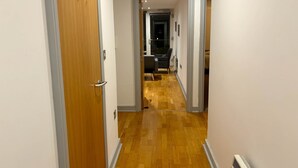 Um corredor com piso de madeira, uma porta à esquerda e uma cadeira ao fundo.