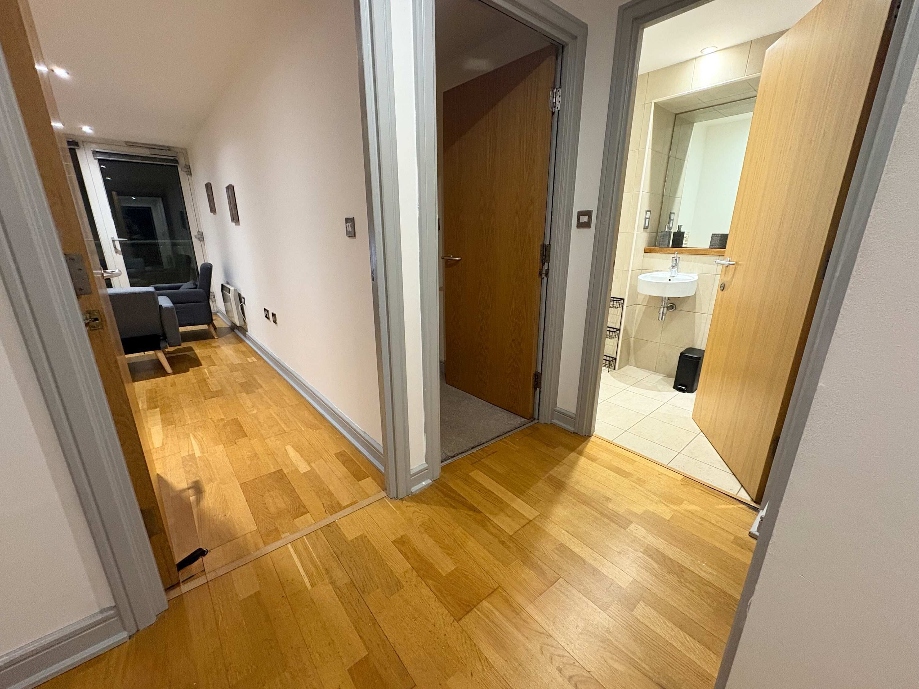 Un couloir avec un plancher en bois, un coin salon avec un canapé et des fauteuils, et une salle de bain avec un lavabo et un miroir.