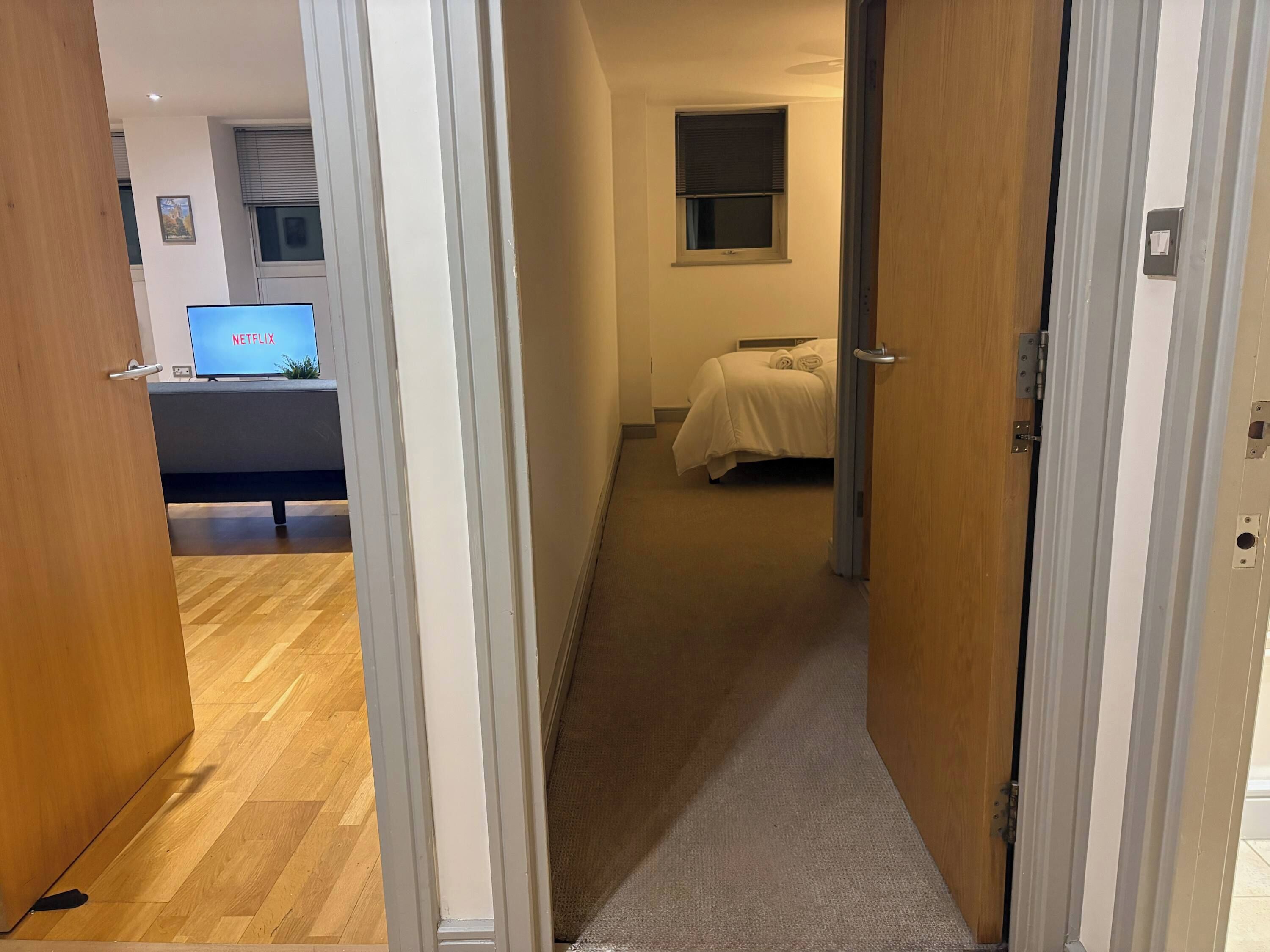 Une chambre d’hôtel avec un lit, un bureau sur lequel se trouve un ordinateur affichant l’écran de « NETFLIX », et une fenêtre avec des stores.