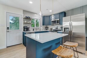 A modern kitchen with a central island, stainless steel appliances, and blue cabinetry. - Adventure Home! Hot Tub, Sauna, Golf, Firepit. Sleeps 10 Near Garden of the Gods (Colorado Springs)