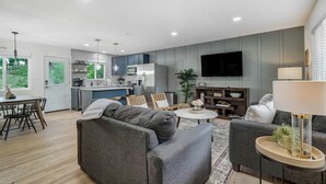 Een moderne woonkamer met een grijze bank, een salontafel en een aan de muur bevestigde televisie.