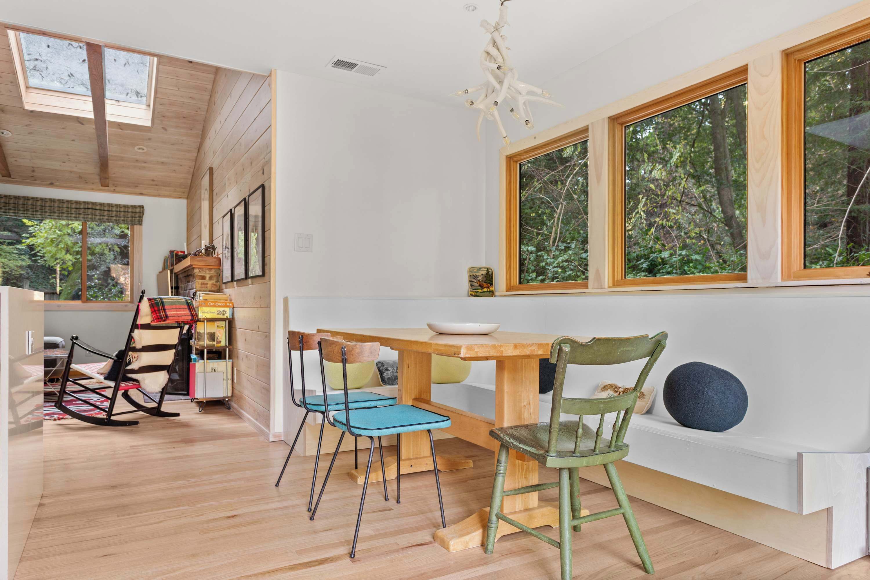 A modern kitchen with a wooden table and chairs, large windows, and a skylight.
