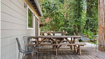 An outdoor patio with wooden picnic tables and metal chairs, surrounded by trees.