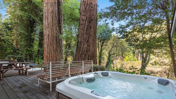 A hot tub on a wooden deck surrounded by tall trees. - Cozy Riverfront Cabin with Dock, Fire Pit & Dogs OK (Monte Rio)