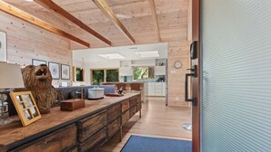A modern kitchen with wooden beams, a large island, and a view of the outdoors. - Cozy Riverfront Cabin with Dock, Fire Pit & Dogs OK (Monte Rio)