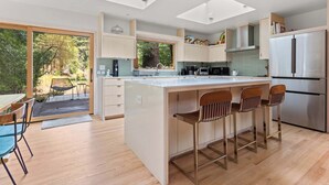 A modern kitchen with a large island, bar stools, and a built-in refrigerator. - Cozy Riverfront Cabin with Dock, Fire Pit & Dogs OK (Monte Rio)