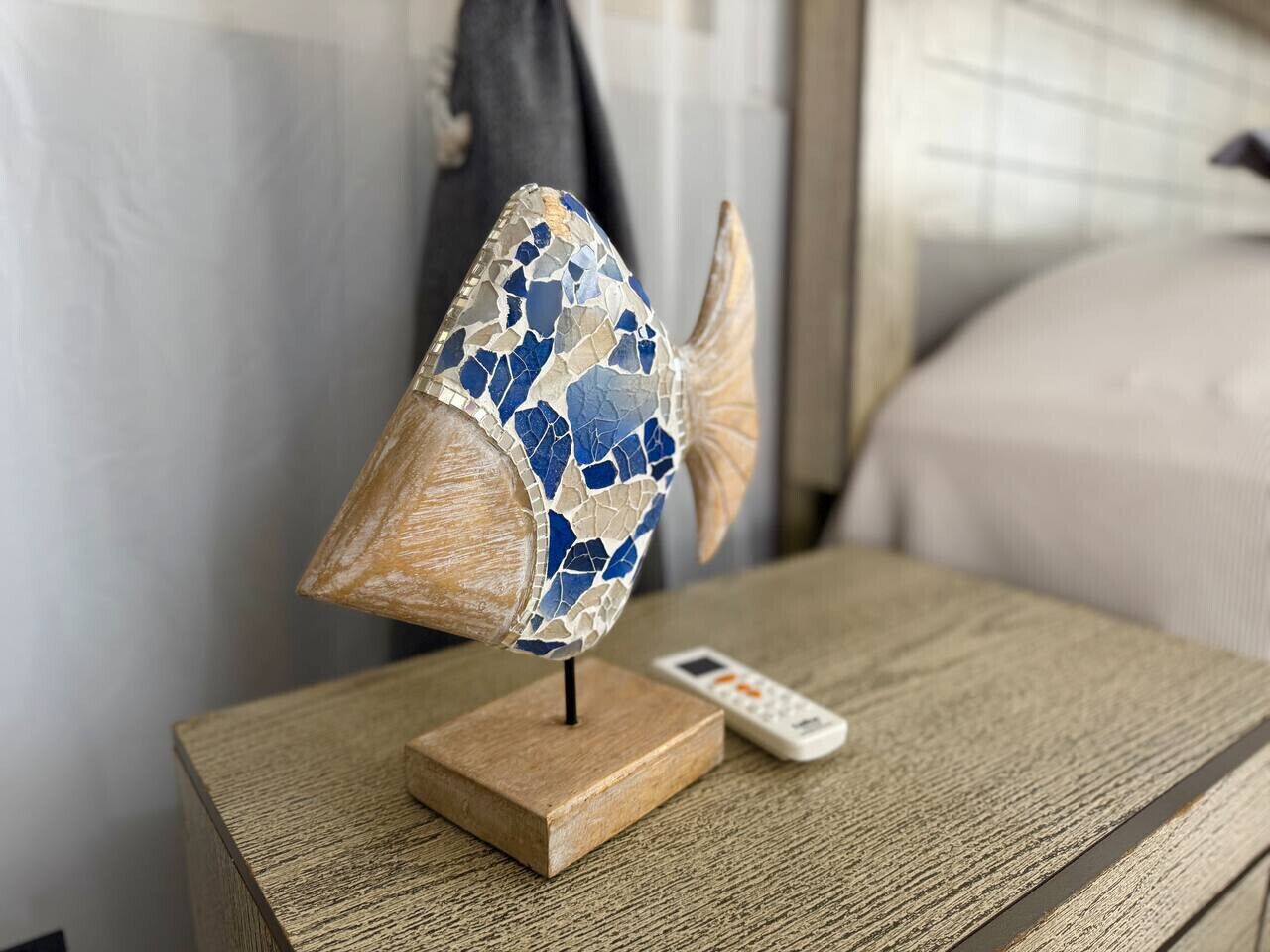 A decorative fish sculpture on a wooden stand with a remote control beside it.