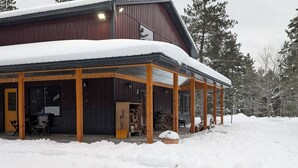 A snow-covered building with a covered porch, wooden beams, and a stack of firewood outside. - Barndominium in RACO, located very close to trails. (brimley)