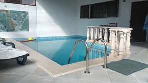 En swimmingpool med ett kaklat poolområde, en solstol och ett dekorativt räcke.