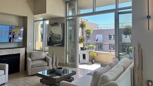 A modern living room with a glass coffee table, a sofa, and a flat-screen TV mounted on the wall. - COZY LUXURIOUS UPSCALE 1-BEDROOM PENTHOUSE DOWNTOWN DENVER! (Denver)