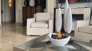 A living room with a sofa, a glass coffee table with a bowl of black pebbles and a small fire, a flat-screen TV mounted on the wall, and a fireplace. - COZY LUXURIOUS UPSCALE 1-BEDROOM PENTHOUSE DOWNTOWN DENVER! (Denver)