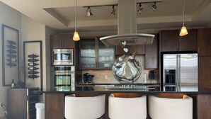 A modern kitchen with stainless steel appliances, a central island with bar stools, pendant lighting, and a decorative vase. - COZY LUXURIOUS UPSCALE 1-BEDROOM PENTHOUSE DOWNTOWN DENVER! (Denver)