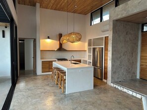 Una cocina moderna con una isla central, taburetes de madera, una lámpara colgante y una pared decorativa de piedra.