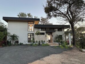 Una casa moderna de dos pisos con diseño minimalista, que presenta un amplio ventanal en la planta baja y una entrada visible.