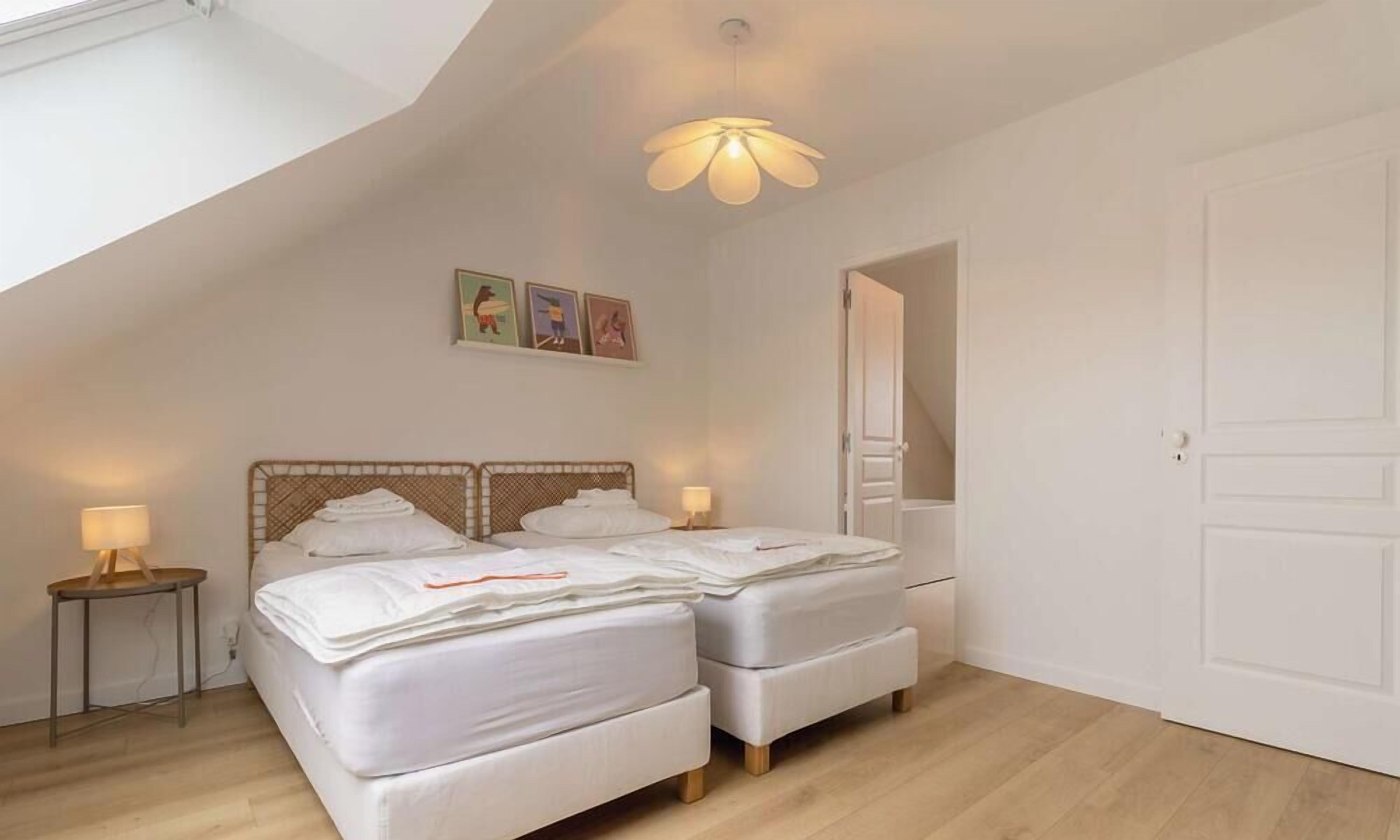 A bedroom with two beds, a sloped ceiling, and a door leading to another room.