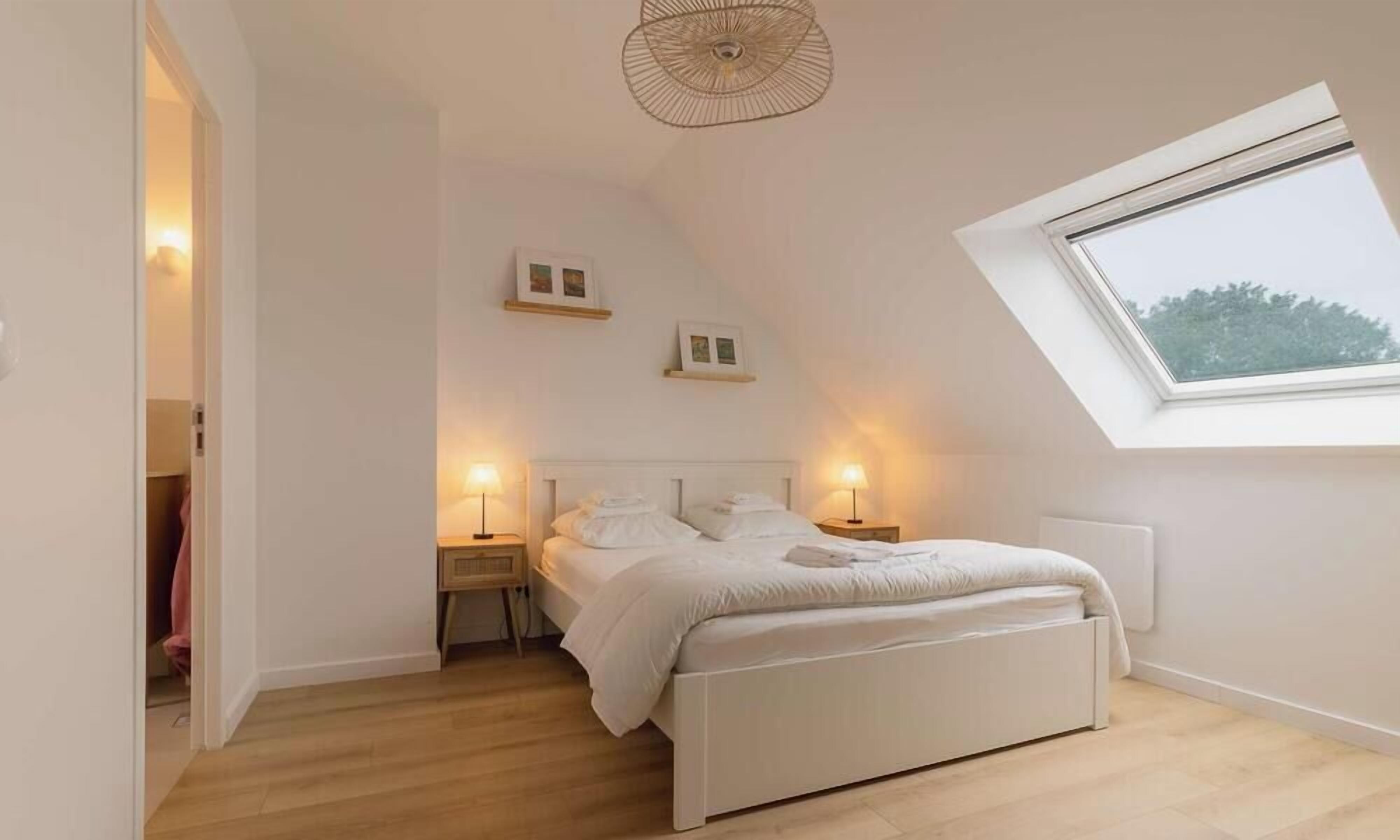 A bedroom with a skylight, a bed, bedside tables, and wall-mounted picture frames.