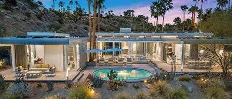 A modern house with a pool, outdoor seating, and palm trees.