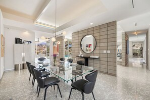 A modern dining area with a glass table and black chairs, a large mirror on the wall, and a view of the outdoors. - Glass Haus - Desert Retreat with Epic Views! (Palm Springs)