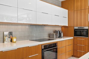 A modern kitchen with white cabinets, a stainless steel range hood, a built-in oven, and a dishwasher. - Glass Haus - Desert Retreat with Epic Views! (Palm Springs)