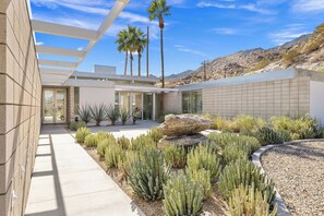 A modern building with a patio area featuring cacti and a rock centerpiece. - Glass Haus - Desert Retreat with Epic Views! (Palm Springs)