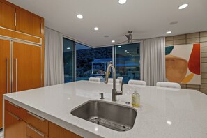 A modern kitchen with a large island, stainless steel sink, and a ceiling fan. - Glass Haus - Desert Retreat with Epic Views! (Palm Springs)