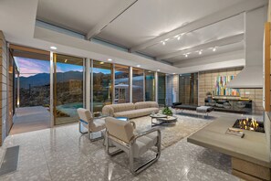 A spacious living area with a large sofa, a coffee table, and a fireplace. - Glass Haus - Desert Retreat with Epic Views! (Palm Springs)