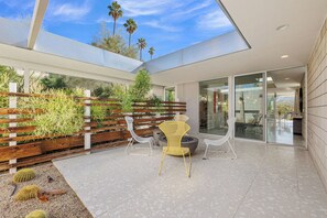 A modern patio with a glass ceiling, a wooden fence with greenery, and a seating area with chairs. - Glass Haus - Desert Retreat with Epic Views! (Palm Springs)