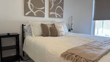 Un dormitorio con cama, almohadas, una mesita de noche y una ventana con vistas.