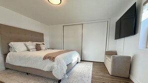 Een moderne slaapkamer met een bed, nachtkastje, een aan de muur bevestigde televisie en een zithoekje.