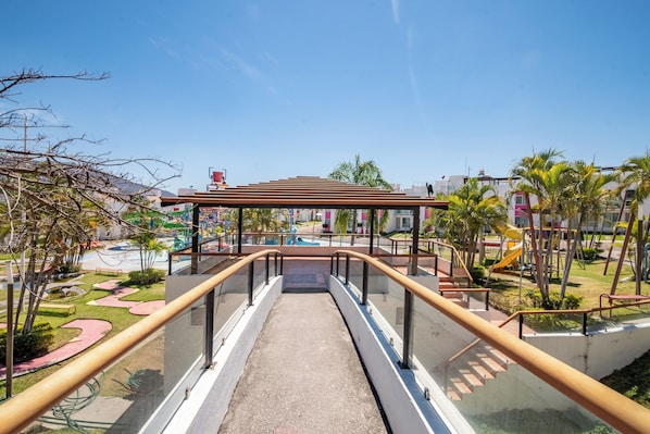 A pathway leading to a playground area with a covered seating area and palm trees.