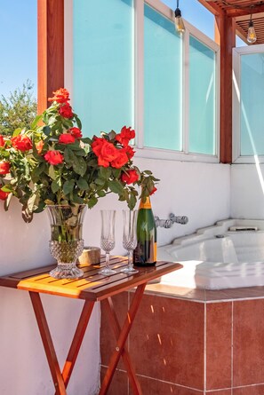 A table with a vase of red roses, champagne bottle, and glasses, near a hot tub and wooden beams.