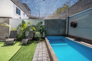 Une piscine dotée d’une terrasse carrelée, entourée d’un mur blanc et d’un espace abrité avec un toit en treillis.