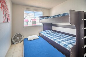 Un lit superposé avec un matelas bleu, un oreiller blanc et une fenêtre avec des stores.