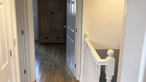 Un couloir doté d’un plancher en bois, de murs blancs et d’une rambarde blanche agrémentée d’une balustrade.