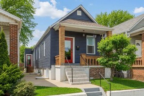 A two-story residential house with a front porch, a red door, and a brick chimney.