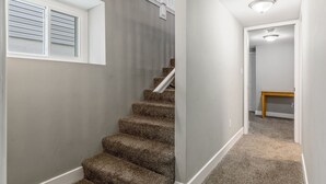 Eine Treppe mit Teppichstufen führt zu einer Zwischenebene, ein Fenster mit Jalousien und eine Deckenleuchte sind zu sehen.