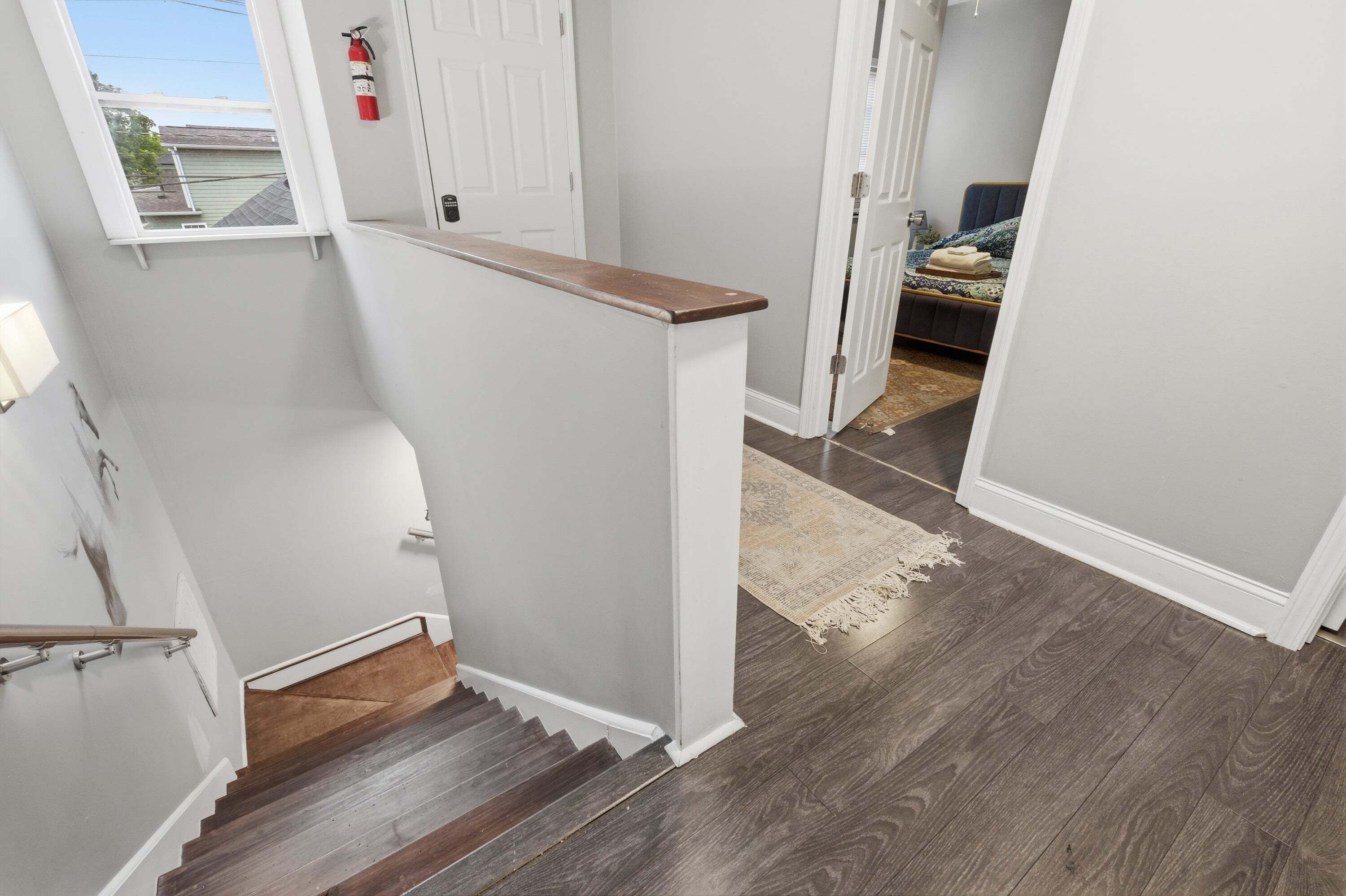 Un escalier avec une rampe en bois, une porte blanche et une vue sur une chambre à coucher avec un lit et un tapis.