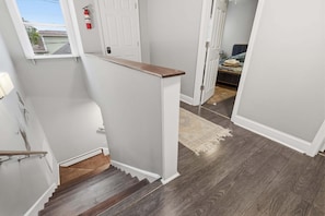 A staircase with a wooden handrail, a white door, and a view of a bedroom with a bed and a rug.